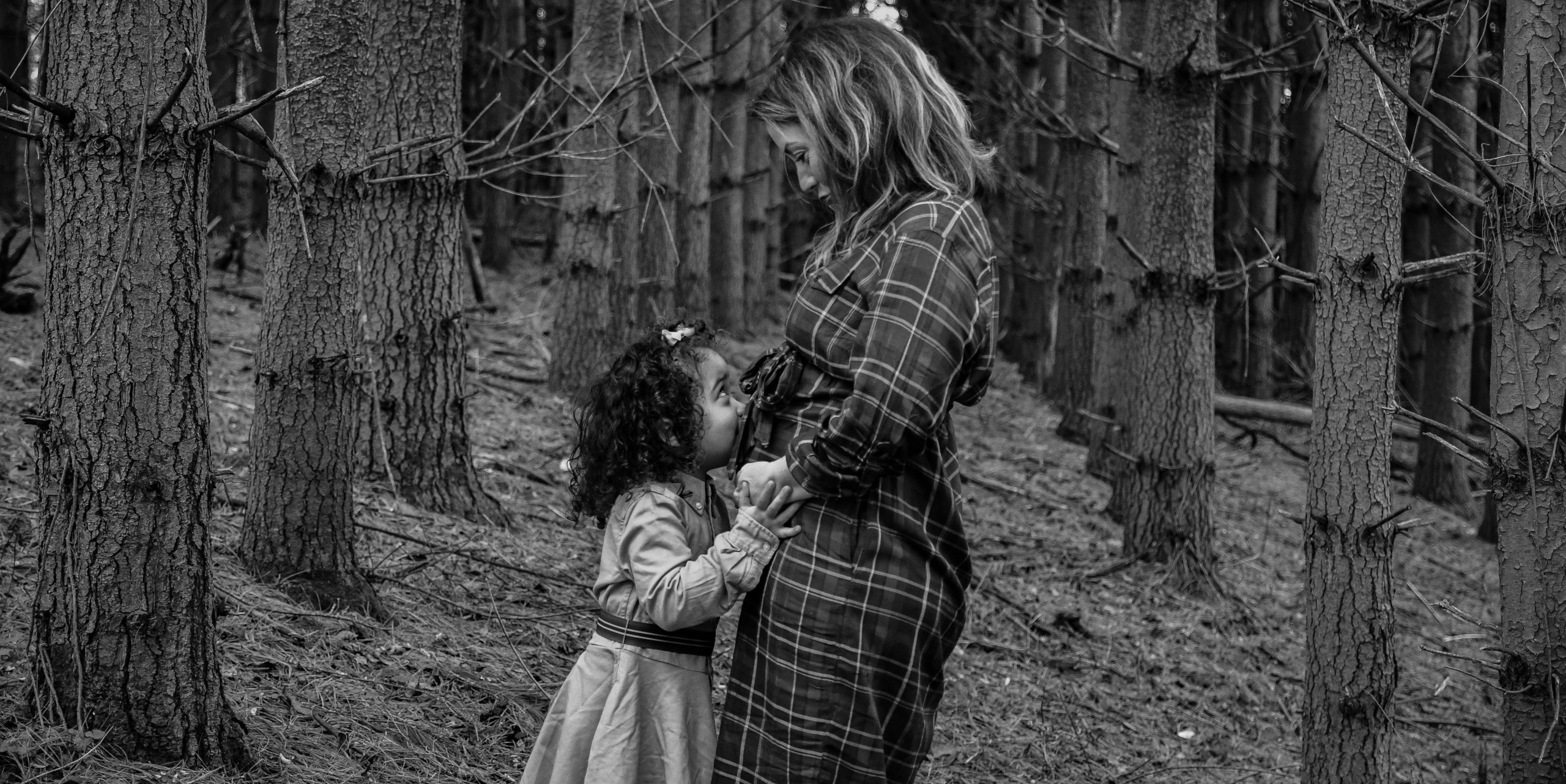 Little girl kissing mother's tummy in forest